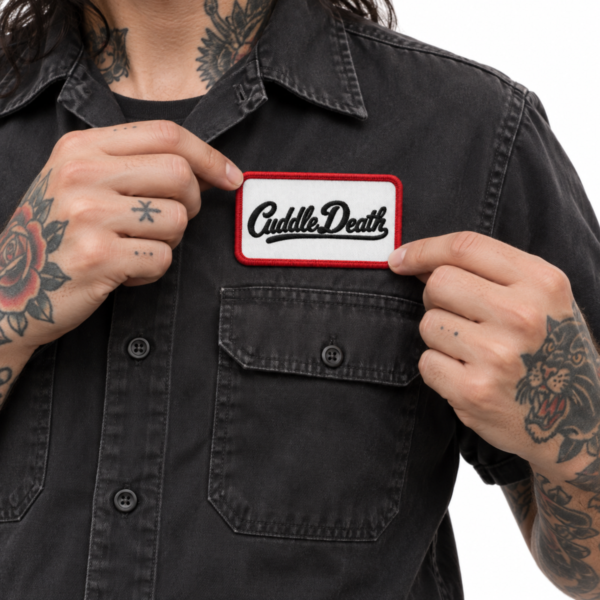 Person positioning the Cuddle Death embroidered patch above the chest pocket of a faded black work shirt.